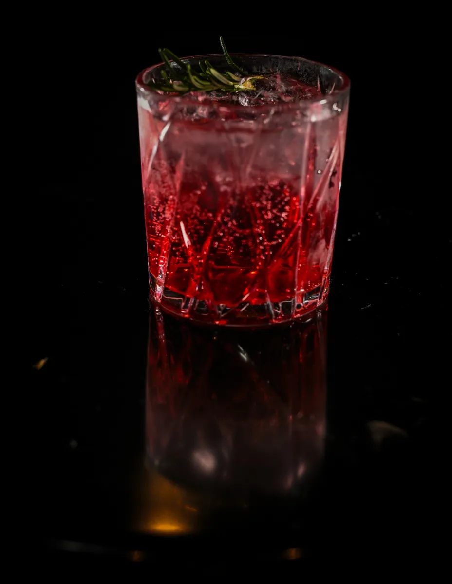 Drink vermelho com alecrim em copo lapidado